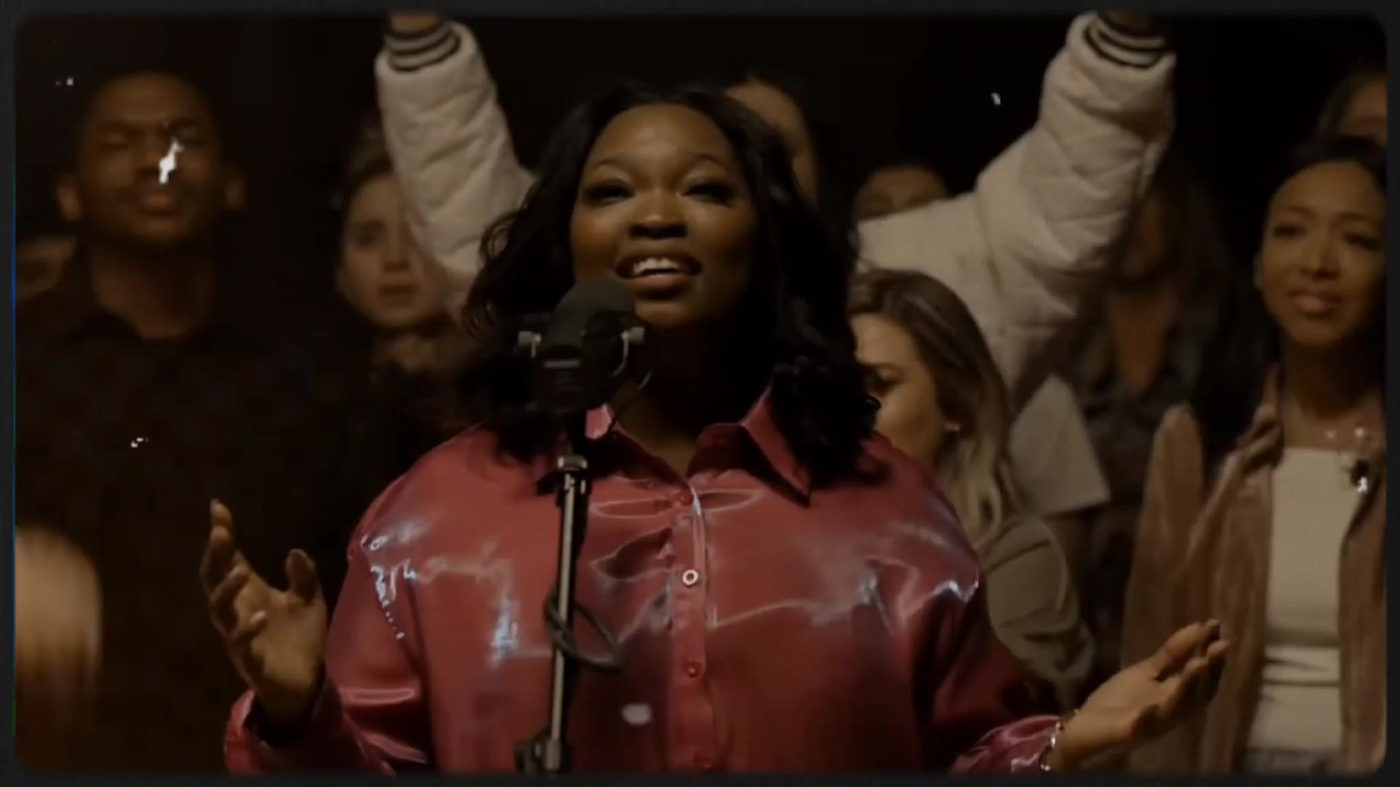 Lou Taylor singing at a microphone in front of a choir