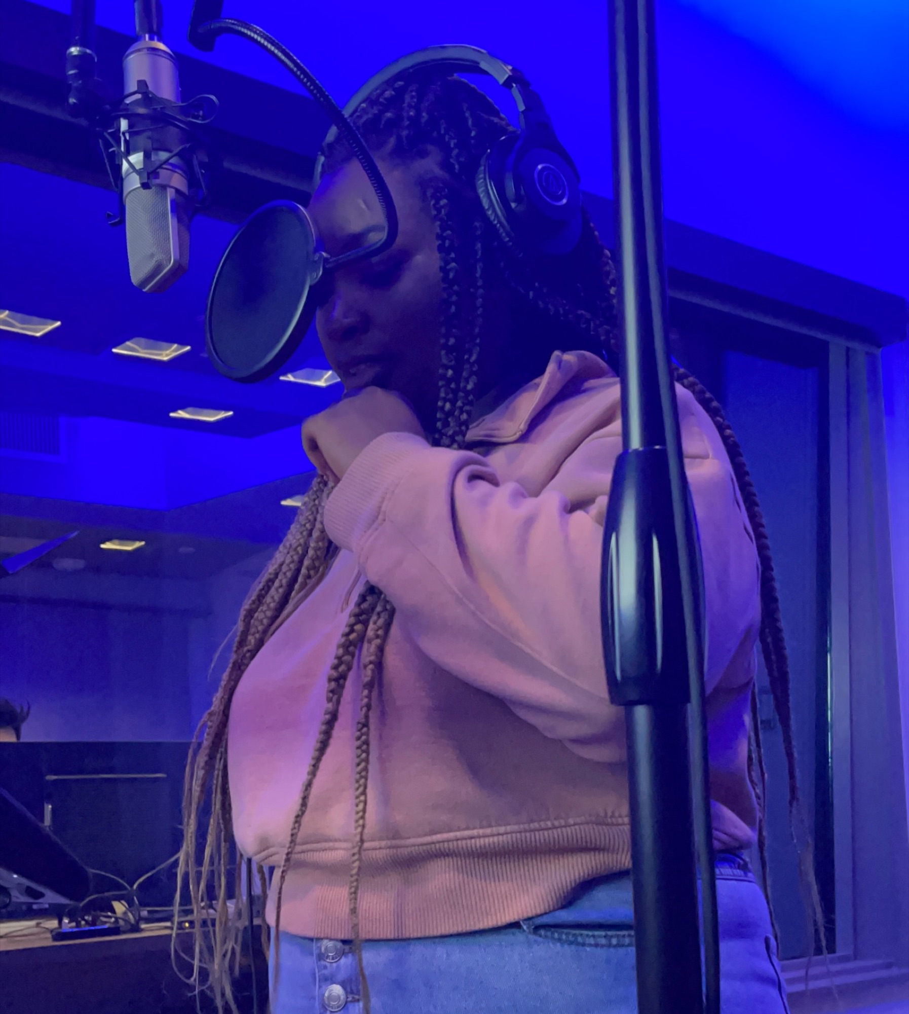Lou Taylor in headphones at a studio microphone, eyes lowered, under blue light